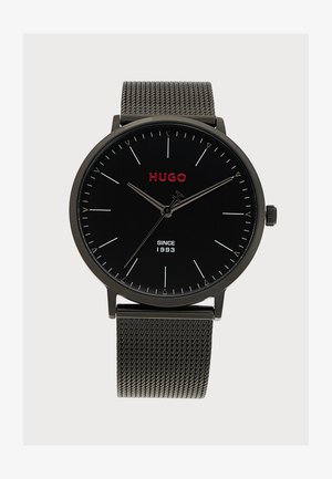 Montre-bracelet noire Hugo avec logo rouge, fines marques d'heure argentées, aiguilles fines argentées et bracelet en métal mesh, affichant l'heure 10:09:36.