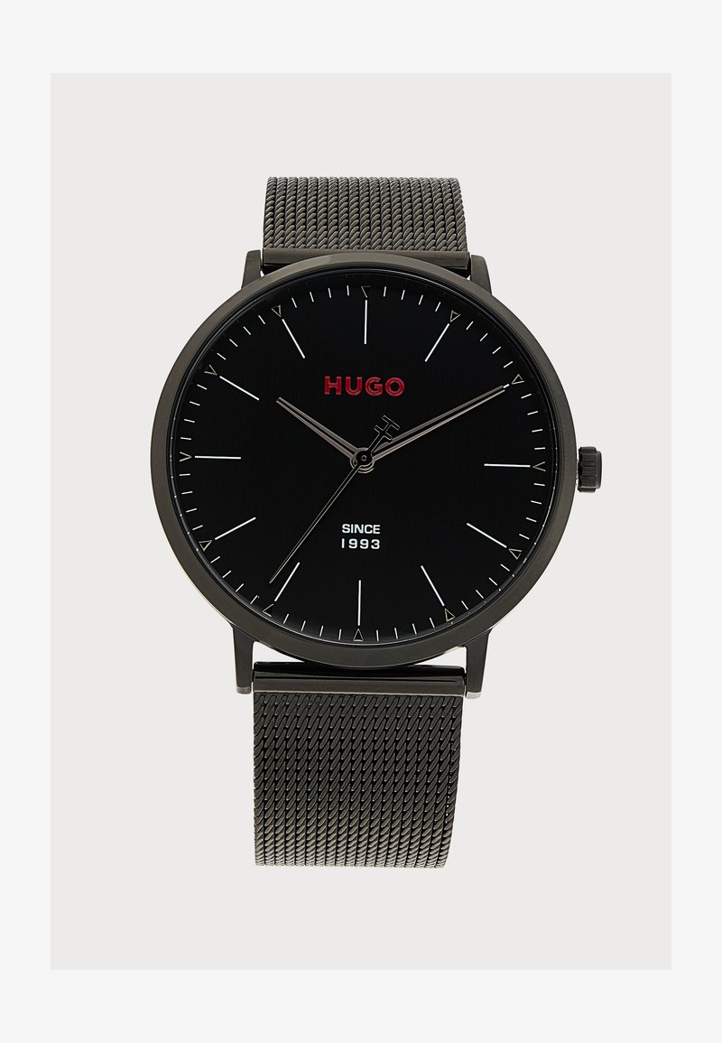 Montre-bracelet noire Hugo avec logo rouge, fines marques d'heure argentées, aiguilles fines argentées et bracelet en métal mesh, affichant l'heure 10:09:36.