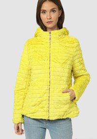 Chaqueta de piel sintética amarilla con cuello alto, con rayas verticales, cremallera frontal y bolsillos laterales. Textura suave y corte relajado.