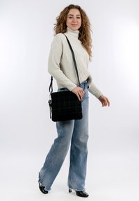 Borsa a tracolla nera trapuntata con design quadrato, caratterizzata da una superficie testurizzata e una tracolla regolabile. Abbinata a un maglione leggero e jeans.
