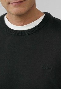 Zwarte gebreide trui met een ronde hals, gelaagd over een witte crewneck t-shirt. Bevat een subtiele s.Oliver-logo in bijpassend donker garen.