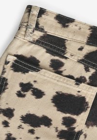 Tissu beige avec motifs éclaboussés noirs, doté de surpiqûres supérieures et d'une poche latérale. Surface texturée avec un léger éclat.