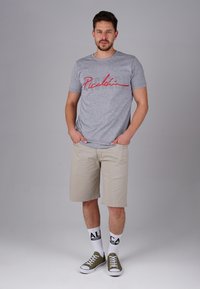 Gray cotton t-shirt with red “Picalo” text, beige shorts, green canvas sneakers, and white socks with black lettering. Standing pose.