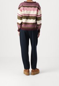 Mönstrad flerfärgad stickad tröja med ränder i rosa, kräm, mörkgrön och vinröd. Kombinerad med lösa marinblå byxor och bruna plattformsskor.