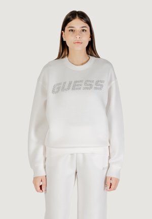 Witte sweater met "GUESS" in zilveren rhinestones. Heeft een ronde hals, lange mouwen en een ontspannen pasvorm. Gecombineerd met bijpassende broek.