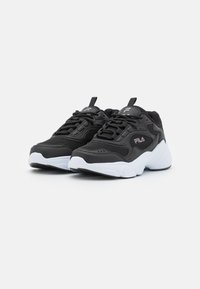 Baskets de sport noires avec des détails en maille, semelle blanche, accents texturés et lacets. Présentent un logo en relief sur la languette et sur le côté.