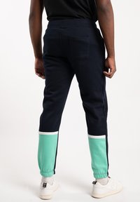 Marina joggers med mintgröna detaljer vid muddarna, vit randdekoration och en bakficka. Tillverkade av ett mjukt, stretchigt tyg.