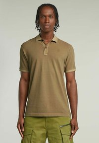 Polo shirt khaki a maniche corte, con colletto a contrasto e patta con tre bottoni. Indossato con pantaloni cargo dotati di numerose tasche.