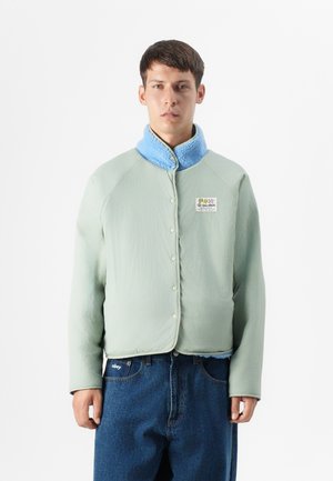 Lichtgroene gewatteerde jas met een blauwe fleece kraag, drukknoopsluiting en een zijzak; heeft een merkembleem op de voorkant.