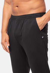 Zwarte joggingsbroek met een elastische tailleband, zijzakken en een klein logo-opdruk aan de linkerkant. Zachte, gladde stoftextuur.