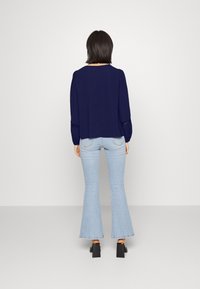 Maglietta a maniche lunghe blu navy con collo arrotondato e dettagli in pizzo ai polsini, abbinata a jeans chiari a campana e scarpe con tacco a blocco nere.