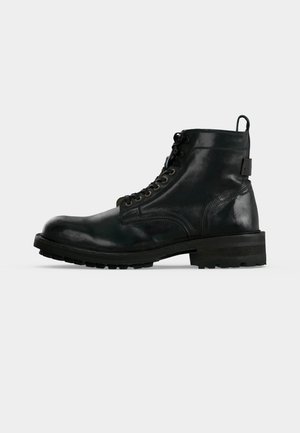 Bottine à lacets en cuir noir avec semelle épaisse et languette à l’arrière, vue de profil sur fond blanc.