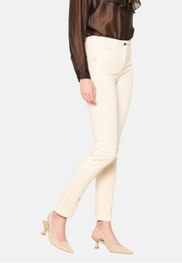 Šviesiai rudos, aptemptos džinsinės kelnės su lygiu paviršiumi, su priekiniais sagų užtrauktukais ir nežymiais siuvinėjimo detalėmis. Pora su permatomu rudu bluzonu.