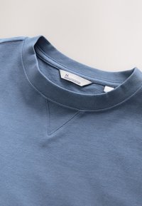 Svetlomodrá mikina s okrúhlym výstrihom a textúrovanou tkaninou. Na krku je malý trojuholníkový doplnok a štítok s nápisom "Premium Collection."