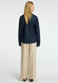 Tamsiai mėlynas džinsinis marškinėlis su apykakle ir ilgomis rankovėmis, derinamas su smėlio spalvos plačiomis kelnėmis. Lygus audinys ir pritaikytas siluetas.