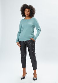 Maglione turchese a maglia con scollatura a coste e dettagli laterali, abbinato a pantaloni neri lucidi slim-fit in ecopelle e décolleté neri con decorazioni.
