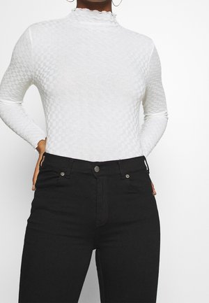 Haut à manches longues blanc avec un motif à carreaux et un col montant festonné, associé à un jean noir taille haute avec des poches avant.