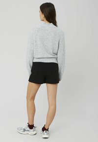 Pull en tricot gris clair avec un ourlet côtelé, associé à un short noir. Le mannequin porte des baskets argentées brillantes avec des accents bordeaux.