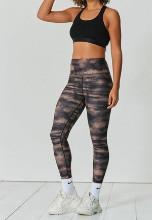 Černá sportovní podprsenka s širokým pruhovaným páskem, kombinovaná s legínami s vysokým pasem zdobenými hnědo-černým tie-dye vzorem a bočními švy.