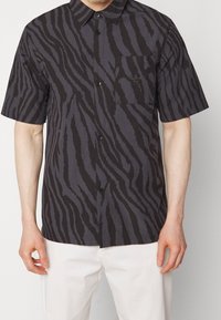 Kortärmad skjorta med knappar i mörkgrått med djärva svarta zebraränder. Har en bröstficka och klassisk krage.