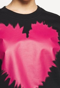 Schwarzes Sweatshirt mit einem großen, unregelmäßigen rosa Herzdesign. Das Herz hat einen Farbverlauf mit sanften Kanten und einer glatten Textur.
