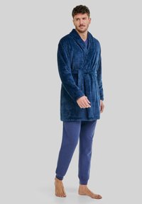 Ropa de color azul marino, texturizada, con cuello de chal y cinturón, combinada con pantalones jogger azules a juego. El material parece suave y esponjoso.