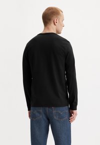 Long-sleeve black cotton shirt with a round neckline and a relaxed fit, paired with blue denim jeans featuring back pockets.