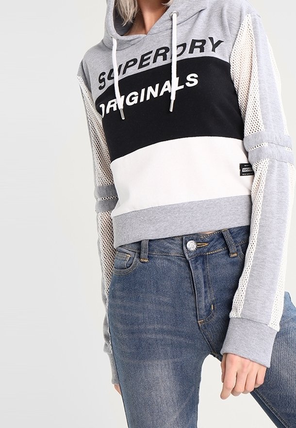 Hoodie court en gris, blanc et noir avec manches en mesh et texte imprimé "SUPERDRY ORIGINALS". Assorti à un jean en denim bleu.