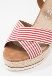 Sangles de sandales rayées rouges et blanches sur une semelle rembourrée beige avec une semelle intermédiaire en jute tressé et une semelle extérieure en caoutchouc blanc.