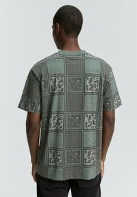 Grøn mønstret kortærmet skjorte med et gitter af dekorative designs, herunder paisleys og geometriske print, lavet af letvægtsstof.