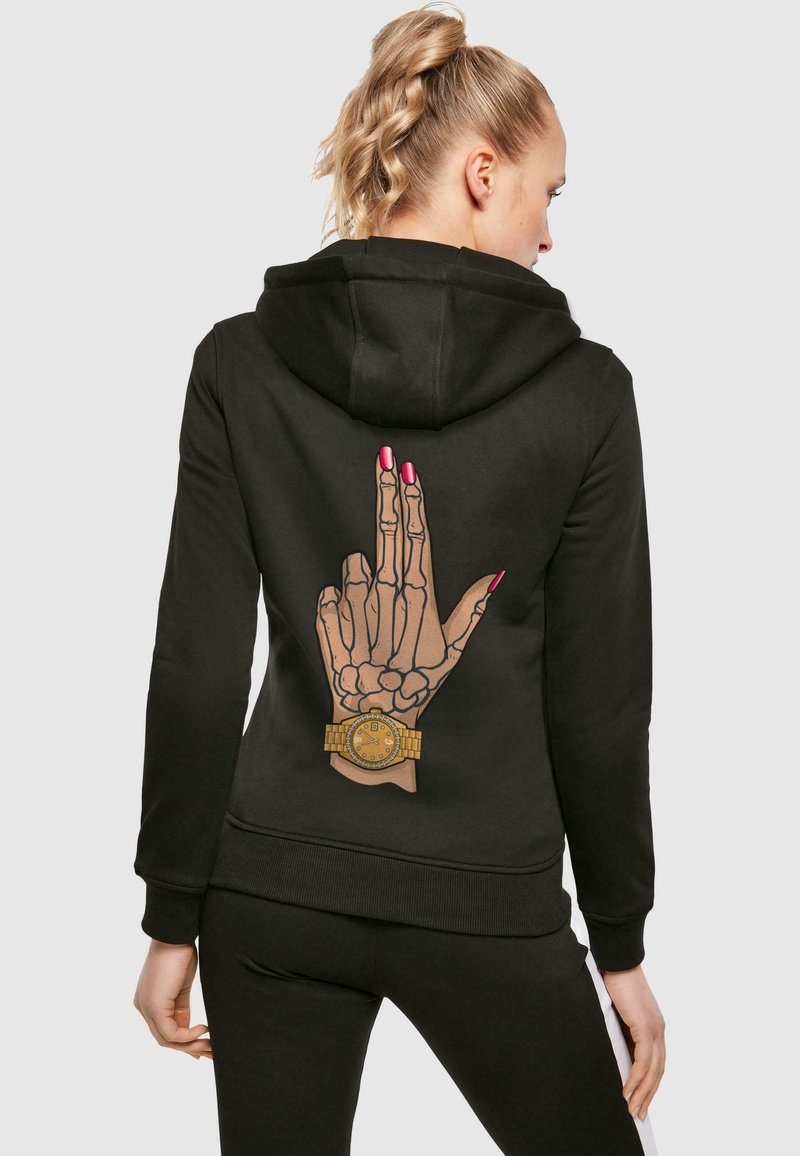 Felpa nera con un grafico dettagliato di una mano scheletrica che mostra un gesto, decorata con un orologio giallo e con unghie rosa.