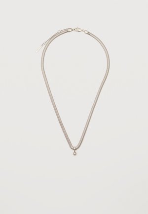 Tynt sølvkjede med et lite, rundt sølvedel, festet med en hummerlås på en enkel hvit bakgrunn.