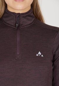 Fittet, lynlåset pullover i mørk maroon, lavet af tekstureret materiale. Har en standkrave og et lille hvidt logo på brystet.