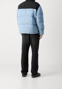 Niebiesko-czarna pikowana kurtka z powtarzającym się wzorem logo, z czarną górną częścią i luźnym krojem, zestawiona z czarnymi spodniami.