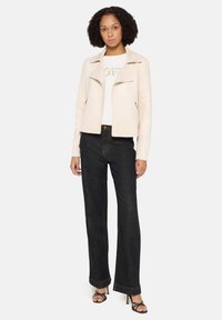 Lichtroze cropped jas met een asymmetrische voorkant, gecombineerd met donkere wijde jeans en zwarte sandalen met bandjes. Soepele textuur en minimalistisch design.