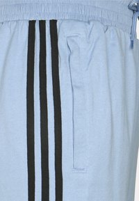 Light blue athletic shorts made of soft fabric, featuring a drawstring waist, side pockets, and three vertical black stripes.