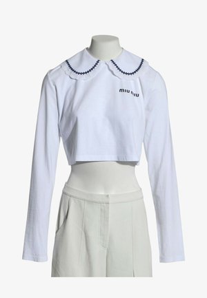 Biały krótki top z długim rękawem, z ozdobnym kołnierzykiem typu Peter Pan wykończonym czarną lamówką i logo "miu miu" na piersi, zestawiony z białymi spodniami z wysokim stanem.