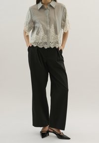 Blusa corta de manga corta en gris claro con rayas verticales y un dobladillo de encaje, combinada con pantalones de pierna ancha negros de cintura alta y zapatos negros de punta.