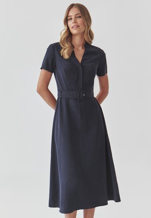 Navy blue dress with a v-neck, short sleeves, belted waist, and flared hem. Smooth fabric with a polished finish.