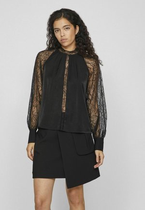 Zwarte blouse met kantmouwen, hoge halslijn en geplooide voorkant. Draag je over een zwarte rok met een overlappend ontwerp en zijzak.