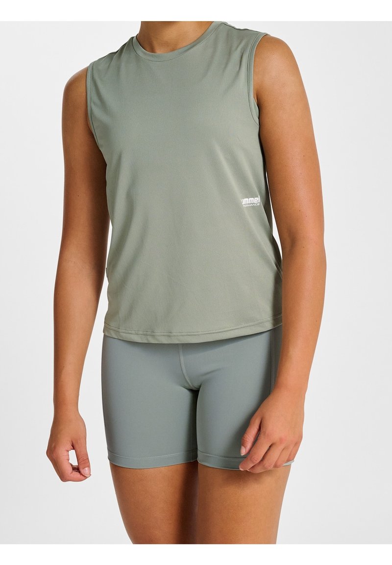 Personne portant un débardeur de sport vert clair sans manches et un cuissard de cyclisme ajusté assorti, debout devant un fond neutre.