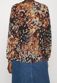 Flerfärgad blus med en blandning av bruna, grå och krämfärgade nyanser samt ett abstrakt djurtryck, långa ärmar och rynkade manschetter.