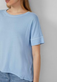 Lichtblauwe t-shirt met korte mouwen, een ronde halslijn en een licht gebogen zoom. Heeft een klein hartlabel aan de onderkant aan de linkerkant.