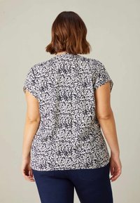 Kortärmad blus i marinblå och vit blommig mönster, med avslappnad passform, mjukt tyg och något rundad sidsöm.