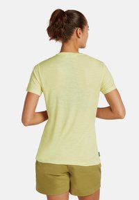 Lys gul kortærmet t-shirt med rund halsudskæring og blød tekstur, parret med olivengrønne shorts, der viser et afslappet fit fra bageste side.