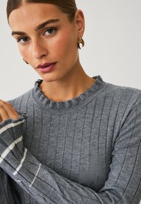 Grauer gerippter Strickpullover mit einem rüschierten Ausschnitt und langen Ärmeln, der weiße gestreifte Akzente an den Ärmelenden aufweist.