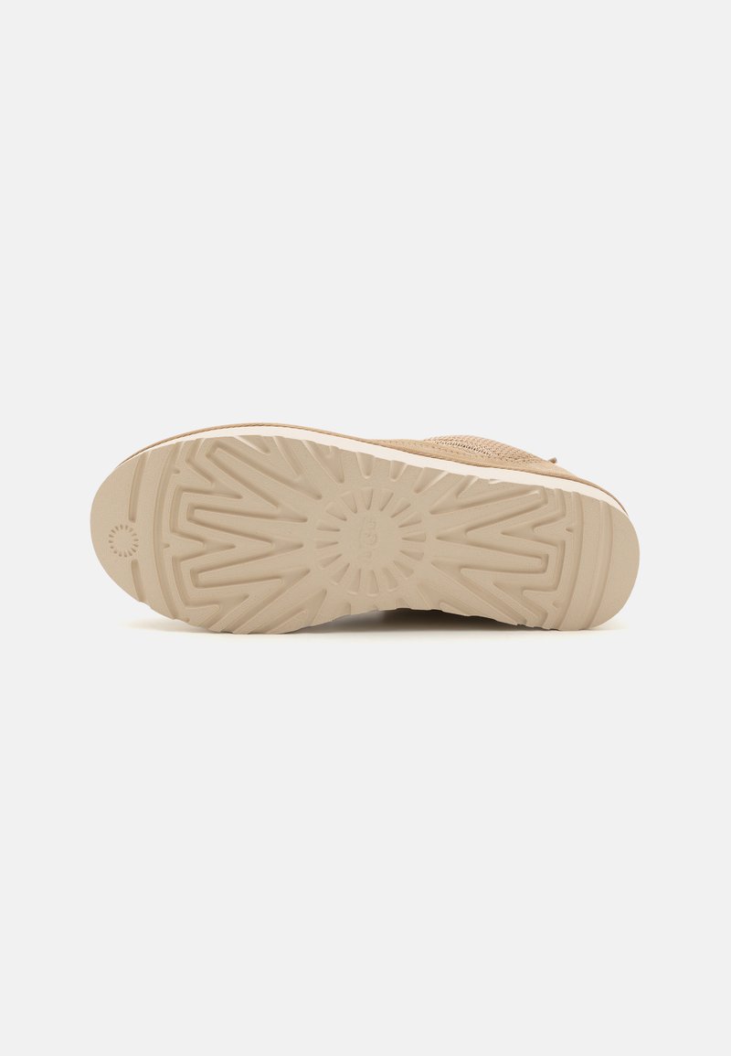 Schuhsohle aus einem strukturierten, beigen Gummimaterial mit einem Sonnenstrahlenmuster und erhöhten Griffen für Traktion.