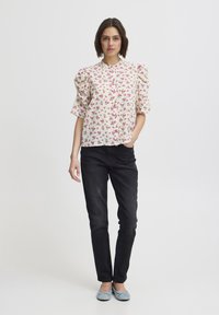 Kremowa bluzka w kwiaty z różowymi motywami, z krótkimi bufkowymi rękawami i guzikami z przodu, zestawiona z czarnymi dopasowanymi dżinsami i niebieskimi balerinami.