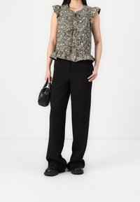 Top peplum floral con mangas rizadas, que presenta un fondo oscuro y patrones en azul y beige. Combinado con pantalones negros holgados y un bolso pequeño.