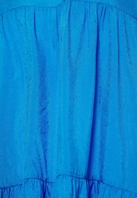 Tissu bleu vif avec un motif texturé subtil, froncé à la taille, avec un détail de ourlet à volants en bas.